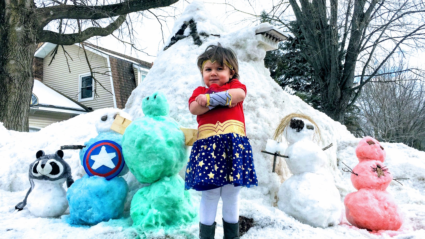 Child Dressed as Wonder Woman Poses with Hero Snowmen