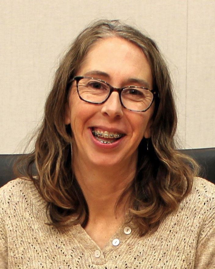 Headshot of person with shoulder length hair, glasses and braces